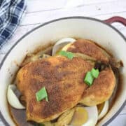 Roasted whole chicken topped with green onions in a Dutch oven with a blue linen behind it
