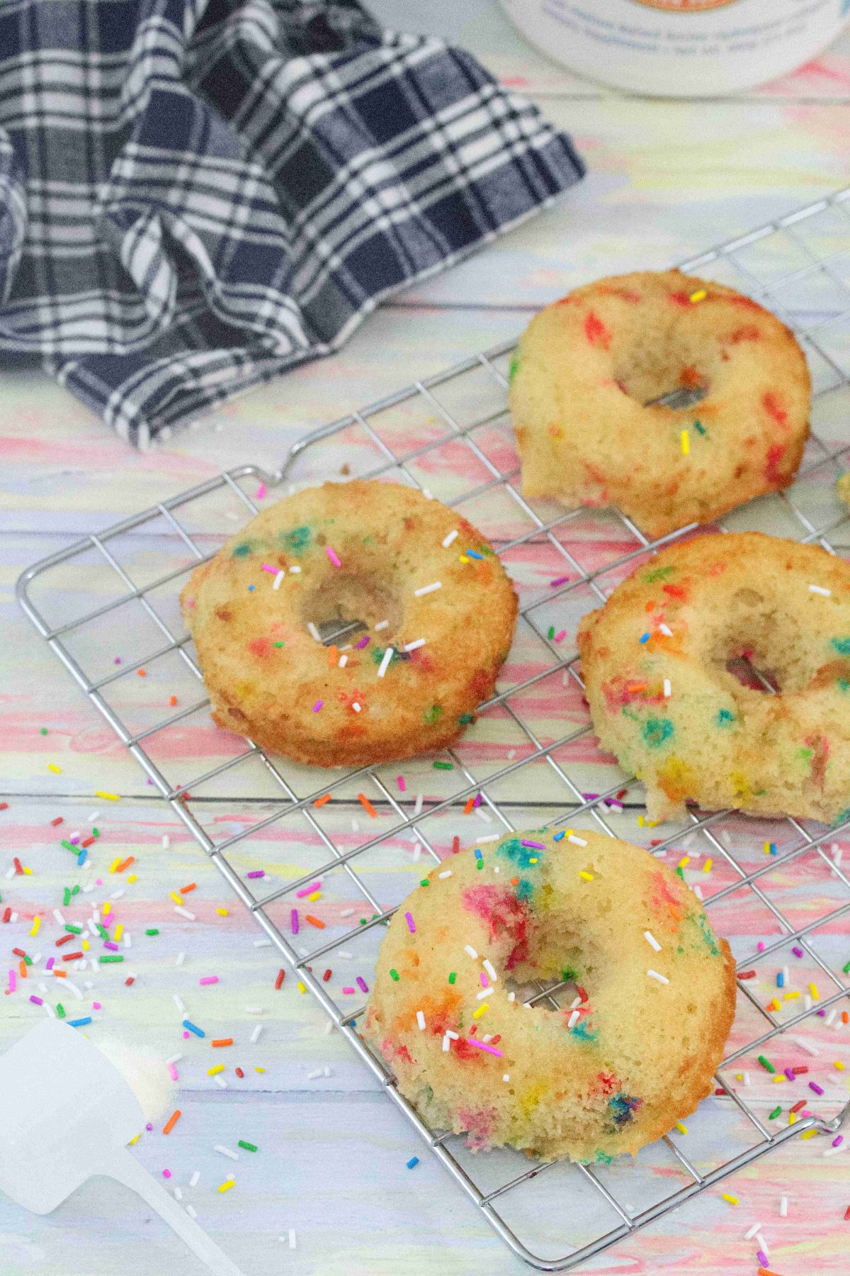 Collagen donuts with sprinkles on a cooling rack with a blue linen behind them and sprinkles around them