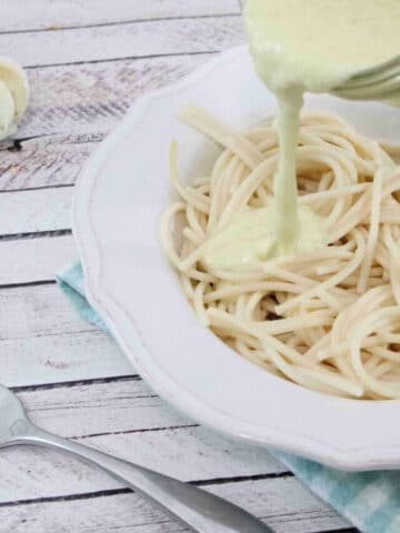 White bowl with noodles in it and coconut milk alfredo sauce being poured on top