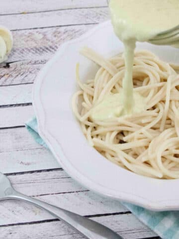 White bowl with noodles in it and coconut milk alfredo sauce being poured on top