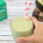 Matcha banana smoothie in a glass with two red straws and a hand holding the glass.