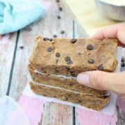 image of three cookie dough protein bars stacked with parchment paper between them and a hand placing the top one