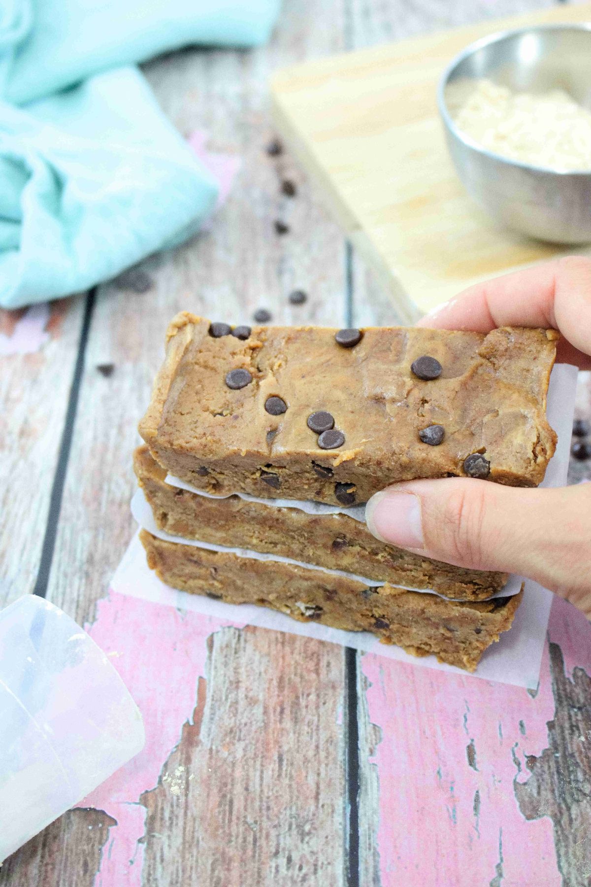 image of three cookie dough protein bars stacked with parchment paper between them and a hand placing the top one.