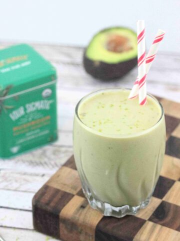 Banana matcha smoothie in a glass with red straws on a checkered wooden currint board.