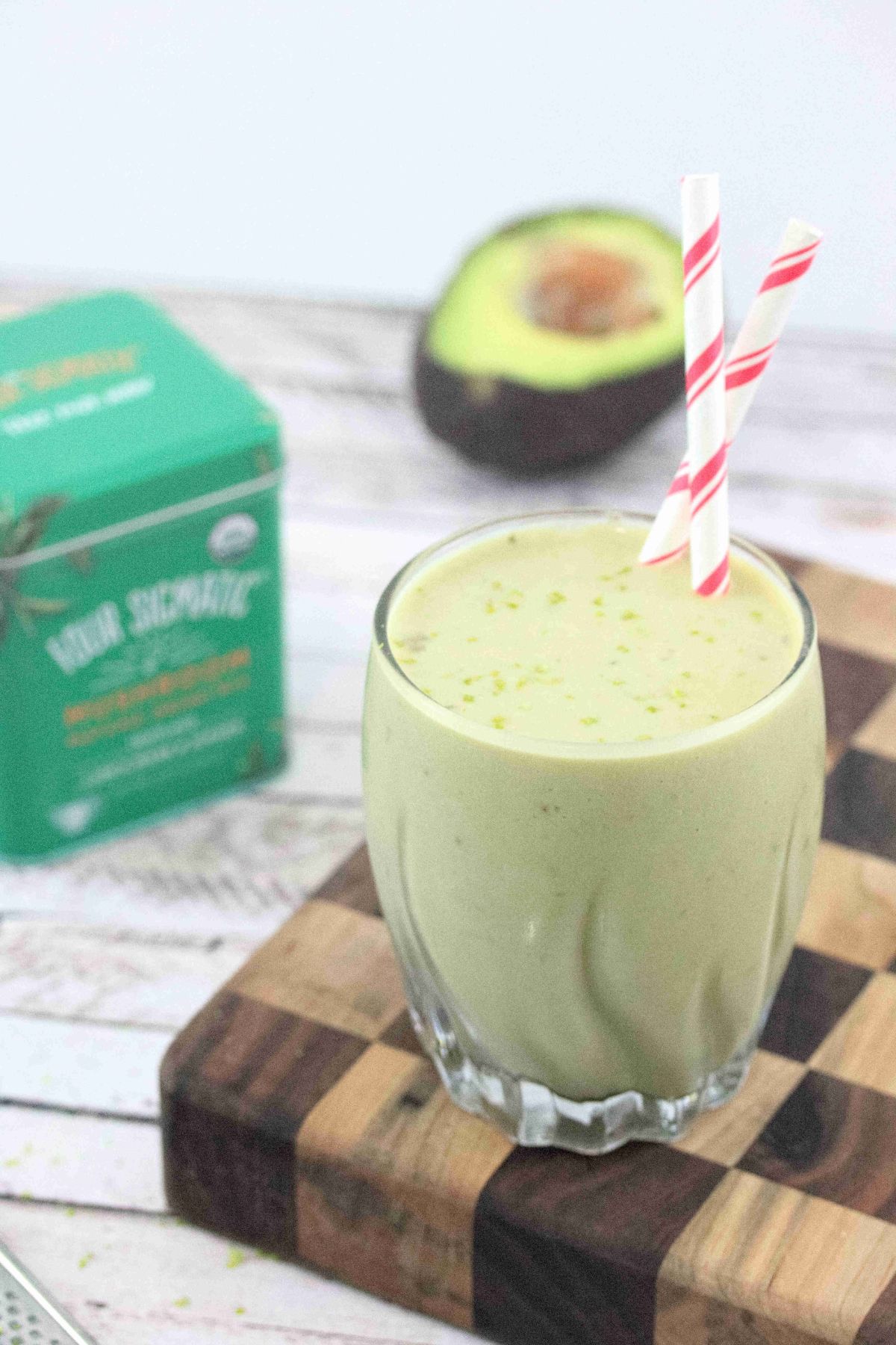 Banana matcha smoothie in a glass with red straws on a checkered wooden currint board.