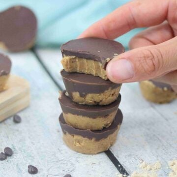 Three peanut butter protein cups stacked on on another with another being placed on top.