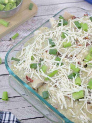 Glass baking dish with chicken alfredo uncooked topped with green onions and dairy-free cheese.