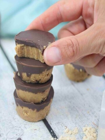 Four chocolate peanut butter cups stacked together with fingers placing the last one with a bite out of it on top