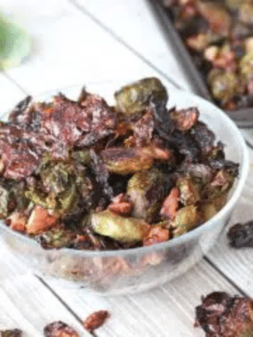 glass bowl with roasted brussels sprouts and more sprouts on a baking tray behind it