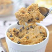 Spoonful of chocolate chip protein cookie dough being pulled out of a white ramekin that's on a wooden cutting board.