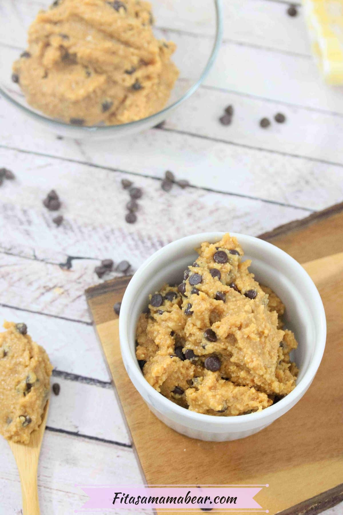 Protein cookie dough with chocolate chips in a white ramekin on a wooden cutting board with cookie dough around it.