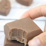 Two fingers placing a square of chocolate protein fudge with a bite out of it on top of another square.