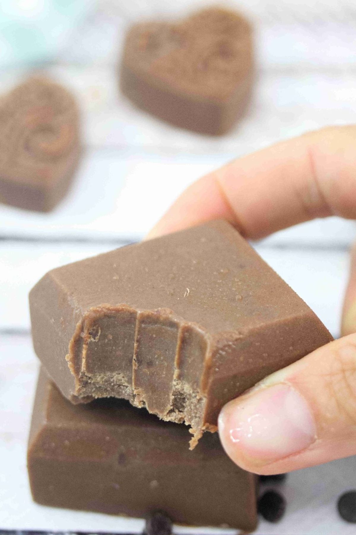 Two fingers placing a square of chocolate protein fudge with a bite out of it on top of another square.