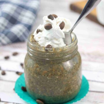 Mason jar with coffee chia pudding topped with dairy-free whipped cream and a spoon in the jar.