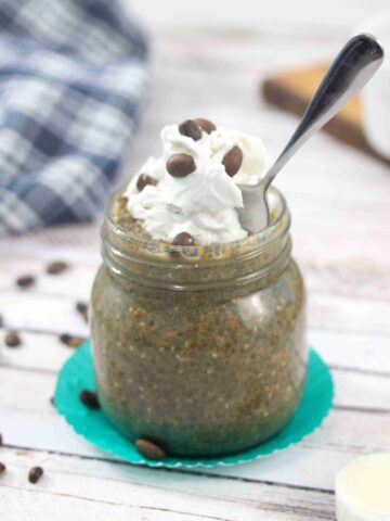 Mason jar with coffee chia pudding topped with dairy-free whipped cream and a spoon in the jar.