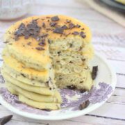 Protein pancakes with chocolate chips stacked on a white and purple plate with a slice cut out of the stack.