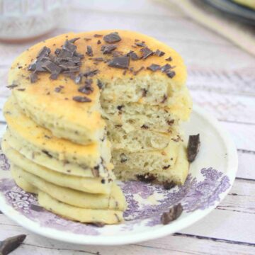 Protein pancakes with chocolate chips stacked on a white and purple plate with a slice cut out of the stack.