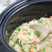 Wooden spoon scooping our dairy-free chicken pot pie from a slow cooker.