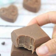 Two fingers placing a square of chocolate protein fudge with a bite out of it on top of another square.