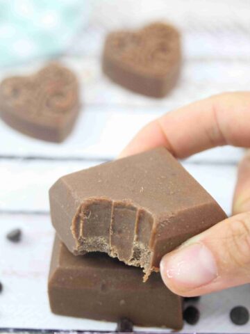 Two fingers placing a square of chocolate protein fudge with a bite out of it on top of another square.