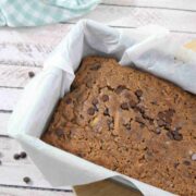 Dairy-free chocolate zucchini bread in a baking loaf with parchment paper and a blue linen and scoop of collagen powder around it.