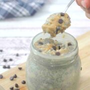 Peanut butter chia pudding with chocolate chips in a mason jar on a cutting board with more chocolate chips around it and a spoon coming out of the mason jar.