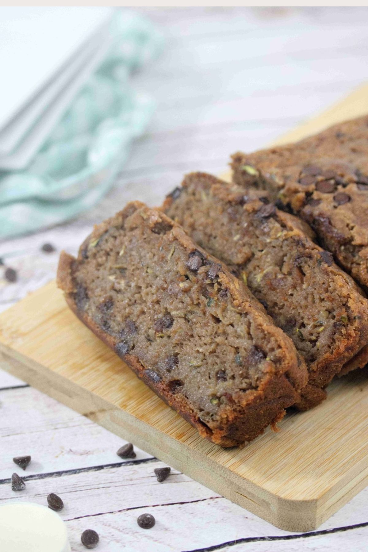 Chocolate protein zucchini bread sliced on a cutting board with chocolate chips around it.