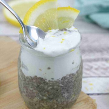 Lemon chia protein pudding topped with coconut cream in a small jar with lemons on top and a spoon in the pudding.