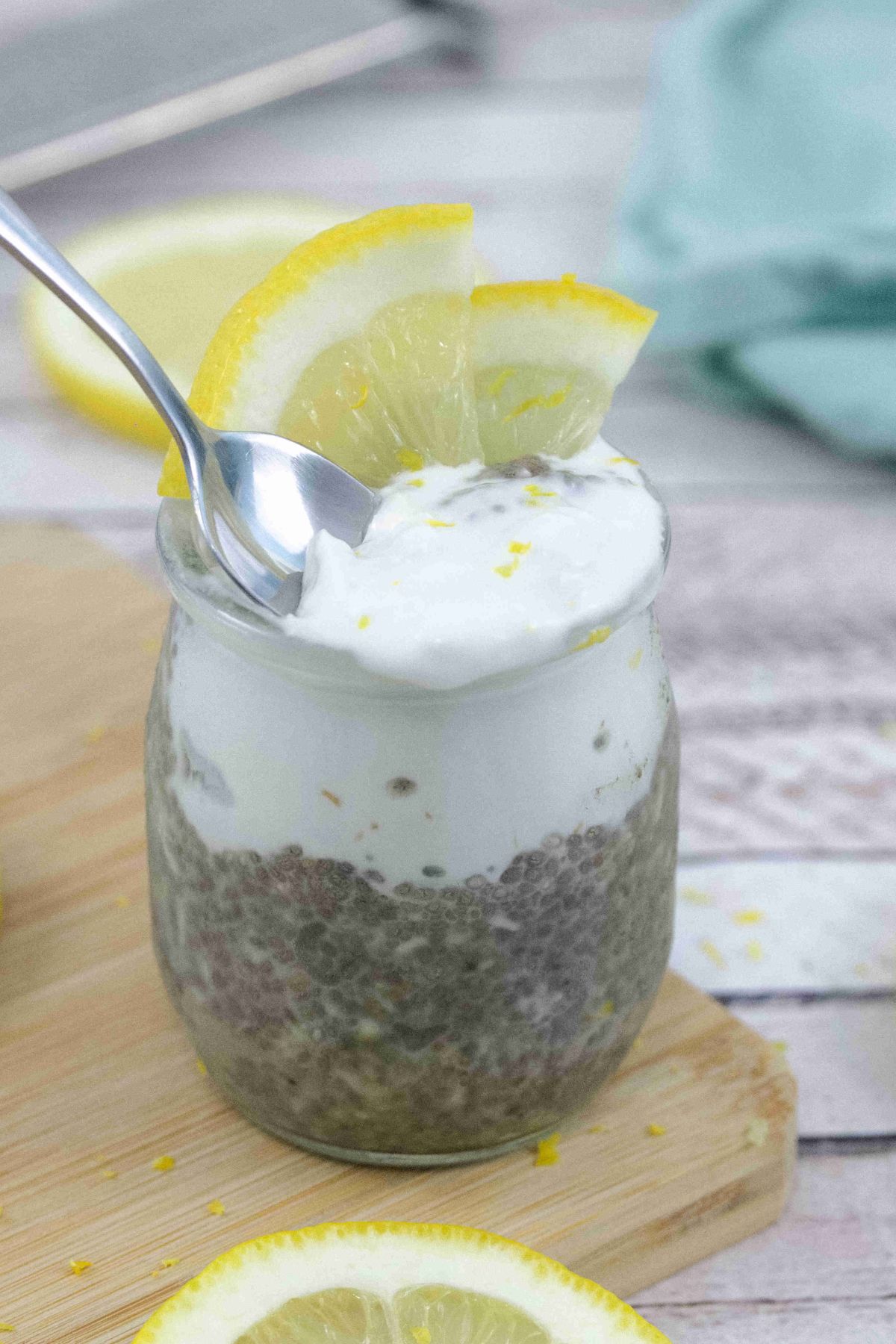 Lemon chia protein pudding topped with coconut cream in a small jar with lemons on top and a spoon in the pudding.