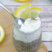 Lemon chia protein pudding topped with coconut cream in a small jar with lemons on top and a spoon in the pudding.