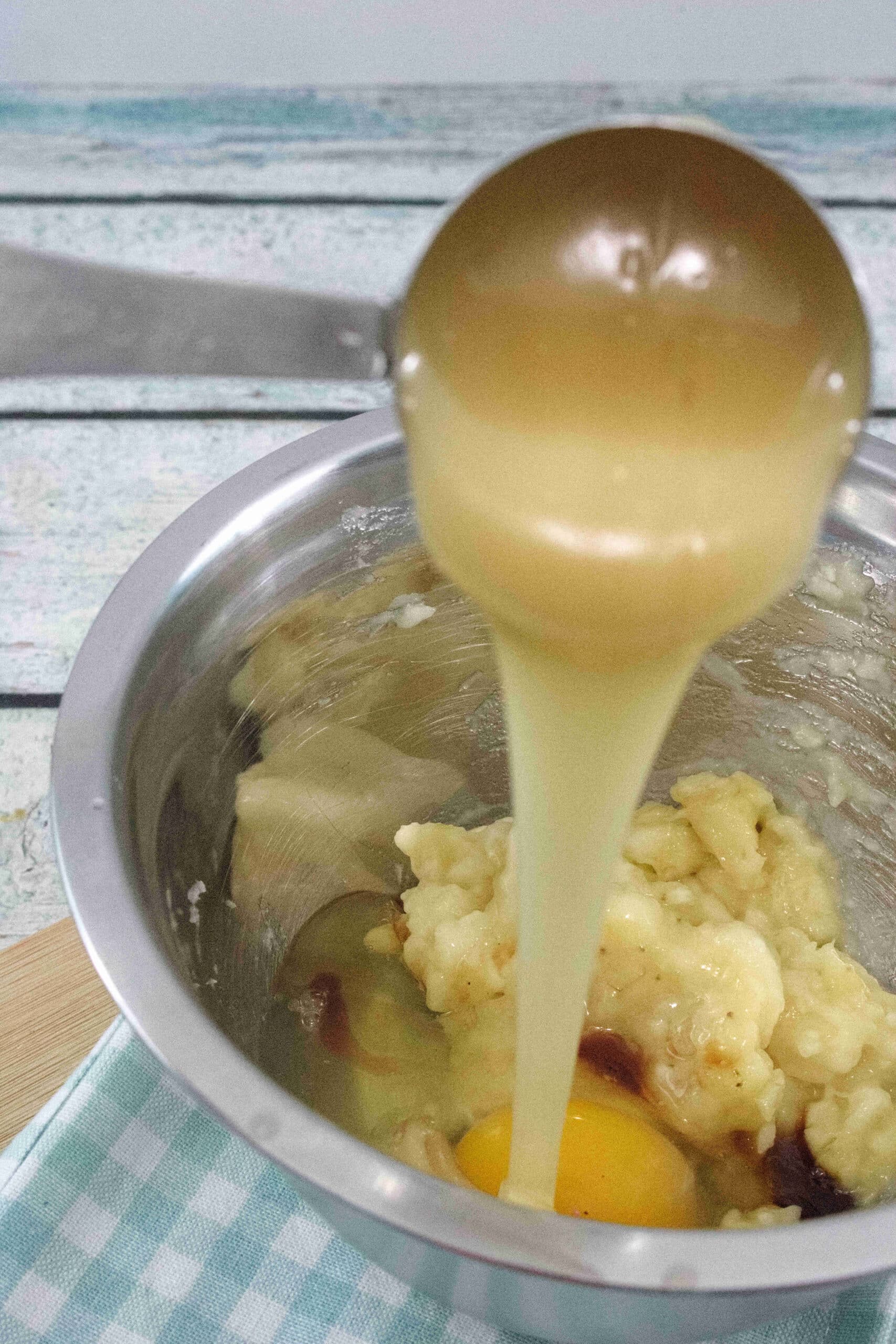 Honey being poured into a steel bowl with mashed banana and egg.