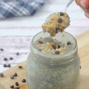 Peanut butter chia pudding with chocolate chips in a mason jar on a cutting board with more chocolate chips around it and a spoon coming out of the mason jar.