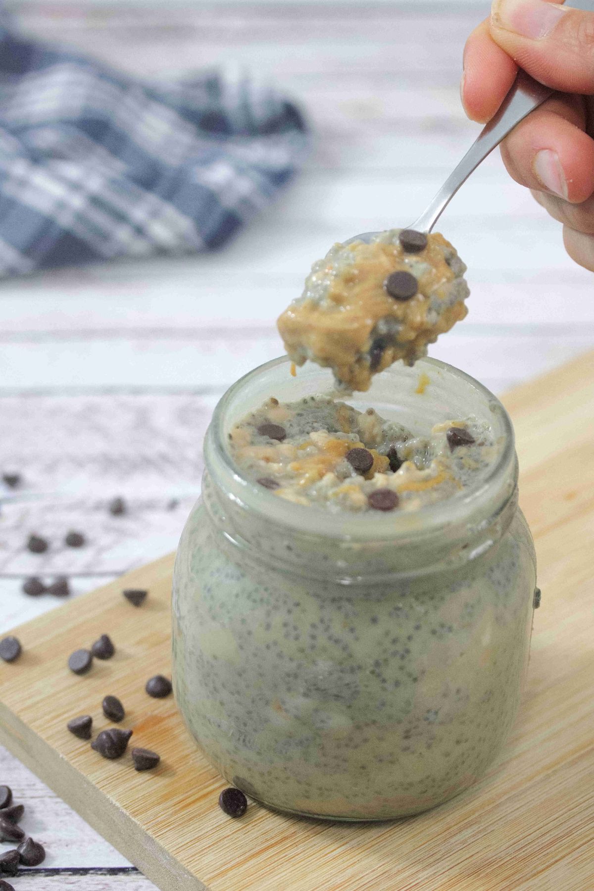 Peanut butter chia pudding with chocolate chips in a mason jar on a cutting board with more chocolate chips around it and a spoon coming out of the mason jar.