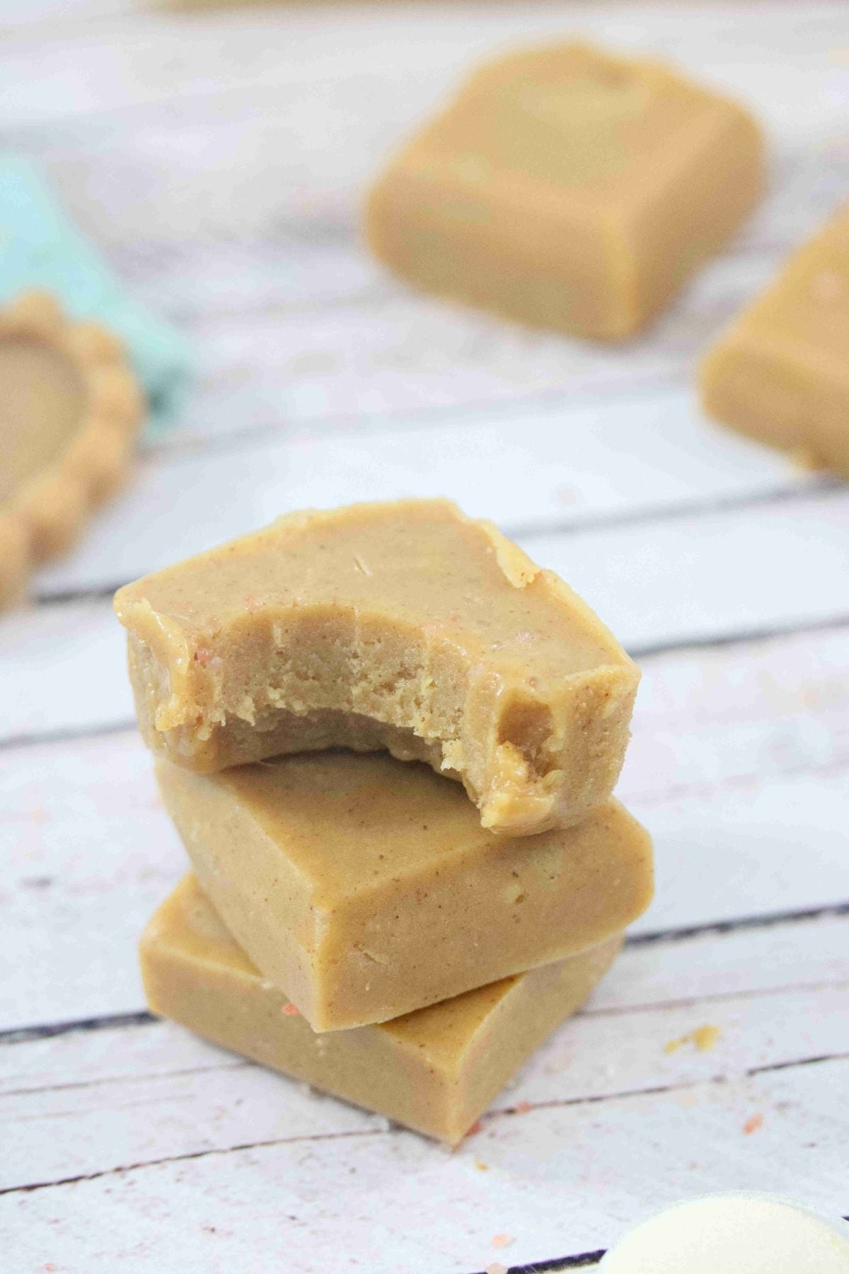 Peanut butter protein fudge squares stakced with a bite out of the top one and more fudge and a jar of honey behind them.