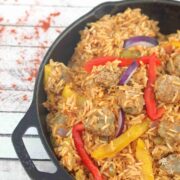 Black skillet with rice, sausages, and peppers in a tomato sauce.