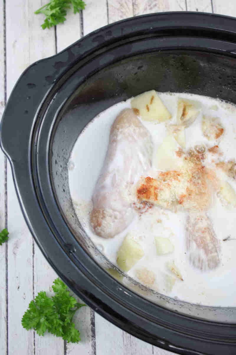 Raw chicken and potatoes in a cream sauce in a slow cooker.