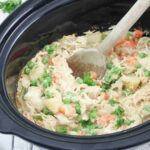 Wooden spoon scooping our dairy-free chicken pot pie from a slow cooker.