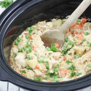 Wooden spoon scooping our dairy-free chicken pot pie from a slow cooker.