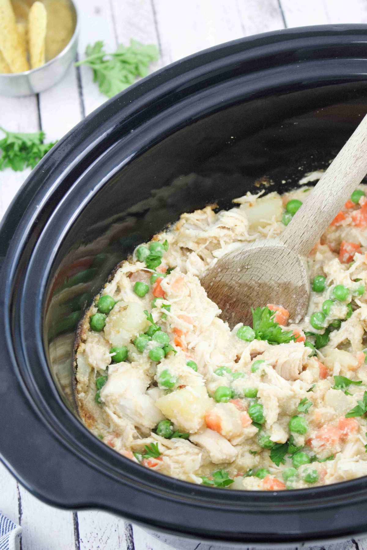 Wooden spoon scooping our dairy-free chicken pot pie from a slow cooker.