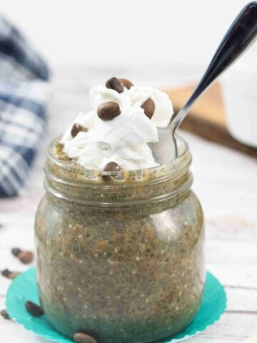 Mason jar with coffee chia pudding topped with dairy-free whipped cream and a spoon in the jar