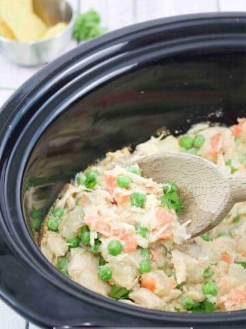 Wooden spoon scooping our dairy-free chicken pot pie from a slow cooker.