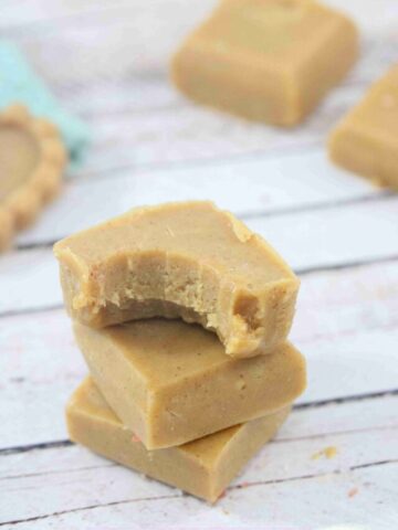 Peanut butter protein fudge squares stakced with a bite out of the top one and more fudge and a jar of honey behind them.