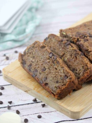Chocolate protein zucchini bread sliced on a cutting board with chocolate chips around it.