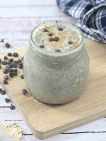 Peanut butter chia pudding with chocolate chips in a mason jar on a cutting board with more chocolate chips around it.