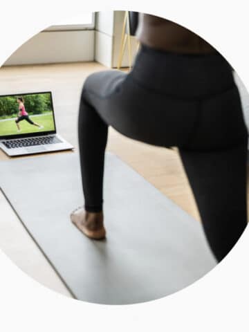 Woman in black pants doing yoga in front of a computer.