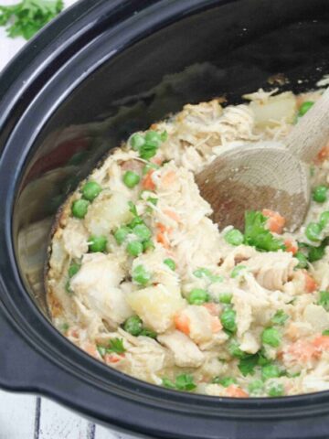 Wooden spoon scooping our dairy-free chicken pot pie from a slow cooker.