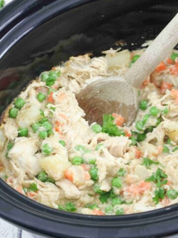 Wooden spoon scooping our dairy-free chicken pot pie from a slow cooker.