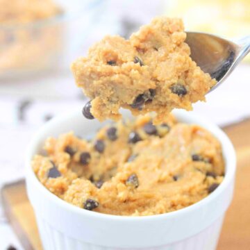 Spoonful of chocolate chip protein cookie dough being pulled out of a white ramekin that's on a wooden cutting board.