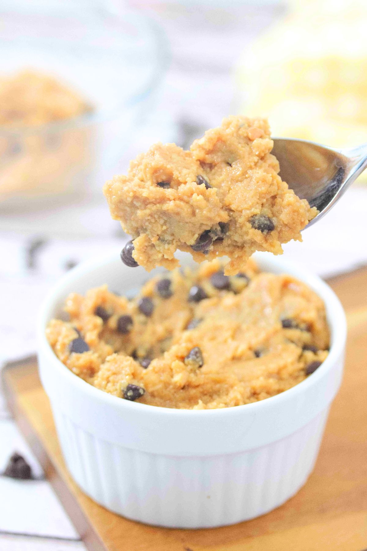 Spoonful of chocolate chip protein cookie dough being pulled out of a white ramekin that's on a wooden cutting board.