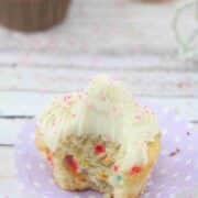 Protein cupcake with dairy-free buttercream frosting on a purple muffin liner with a bite out of the cupcake and more cupcakes behind it.